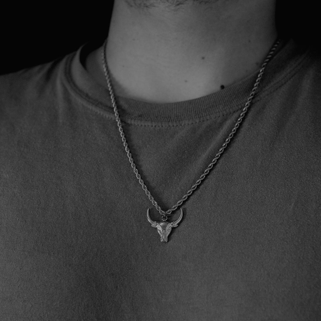 Necklace with a bull head pendant worn by a person on a dark background